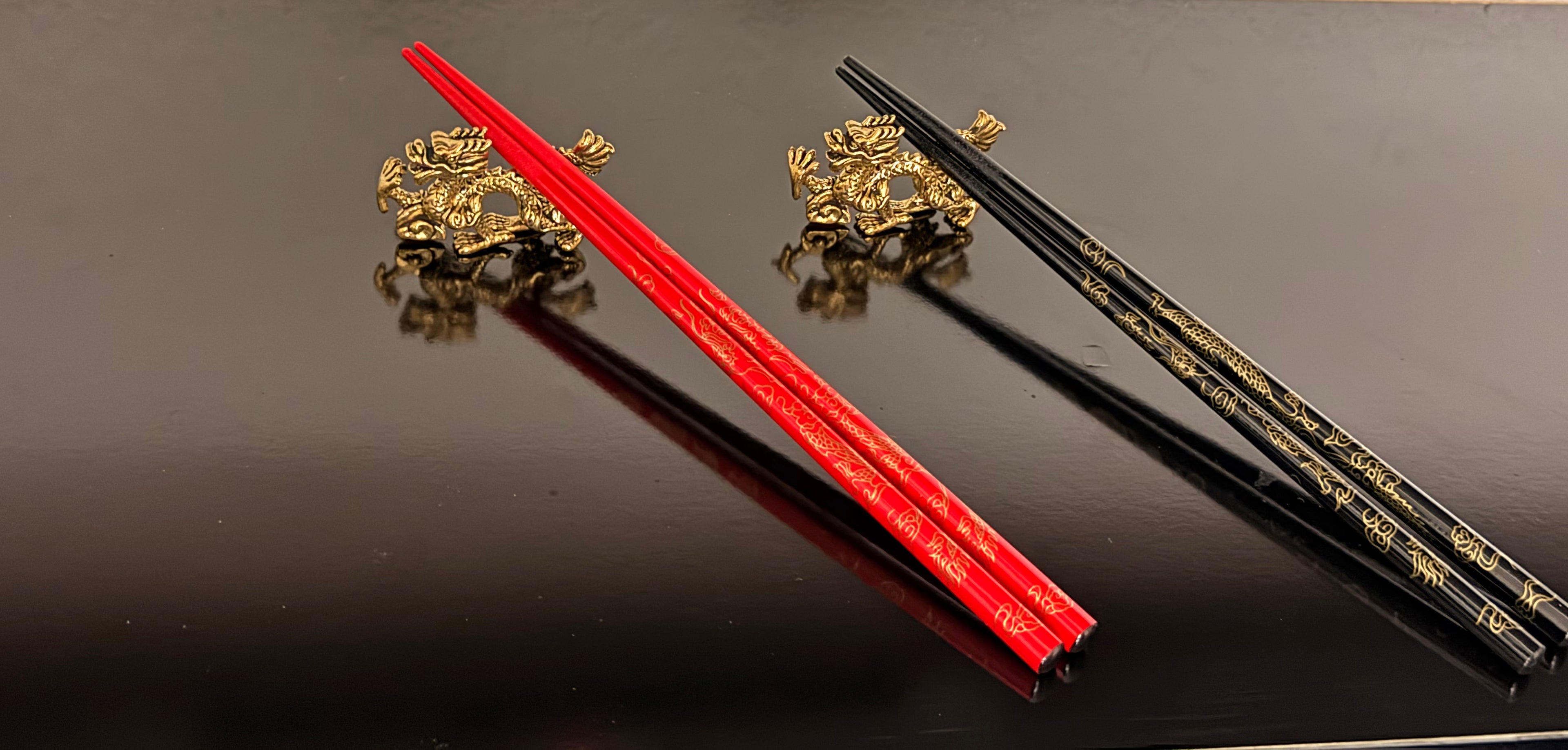 Red and black chopsticks with gold dragon designs on a reflective surface