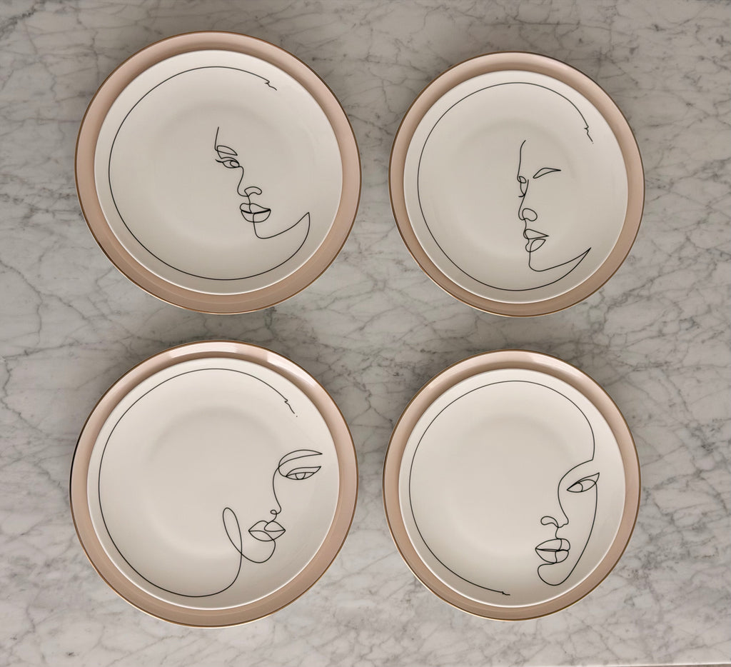 Four ceramic plates with minimalist face designs on a marble surface
